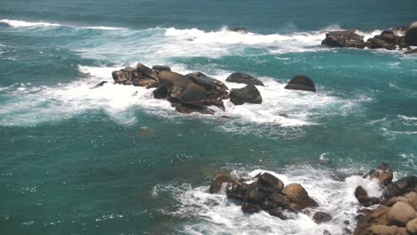 golven die breken tegen een stapel stenen in de blauwe zee van tayrona park, colombia