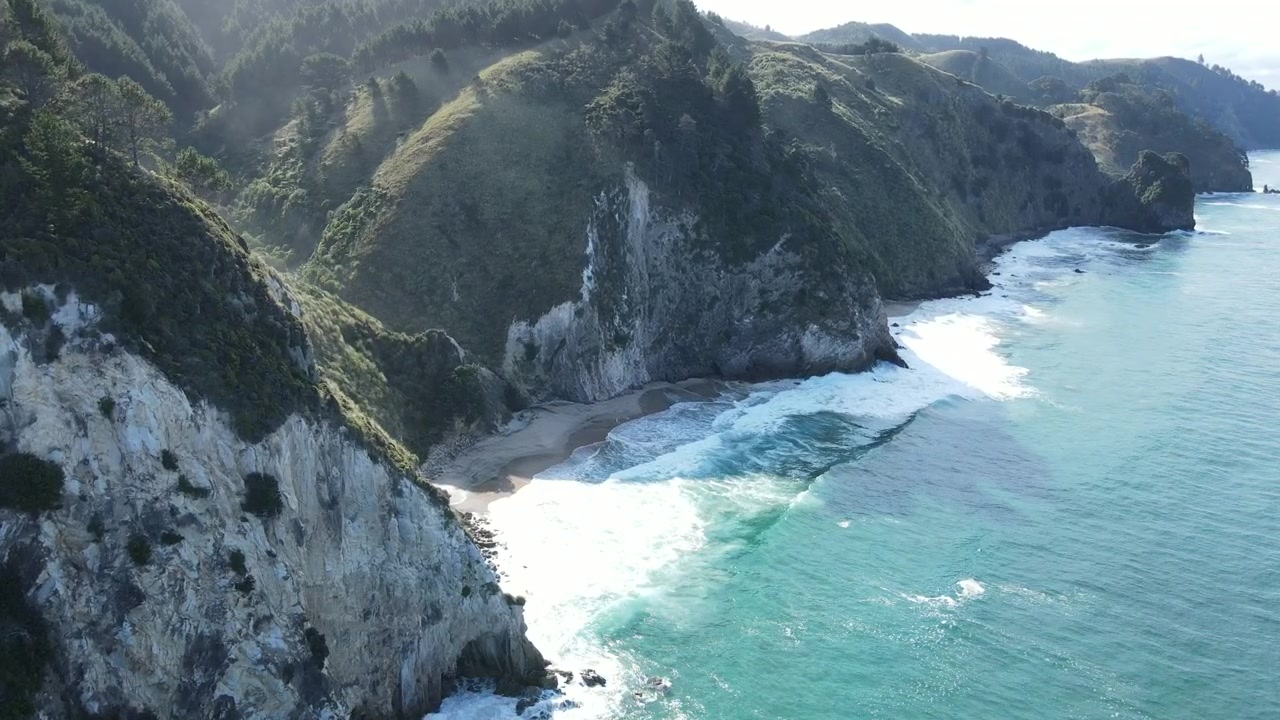 Ripresa con drone in discesa ravvicinata su una piccola spiaggia isolata con onde che si infrangono sulla costa della Nuova Zelanda. 4k 59.94p