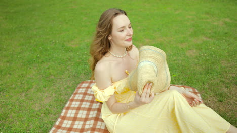 Pretty-Ukrainian-woman-in-yellow-dress-on-picnic-blanket-fans-self-with-hat