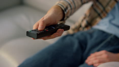 closeup hand zapping tv resting at home. man watching television on sofa alone