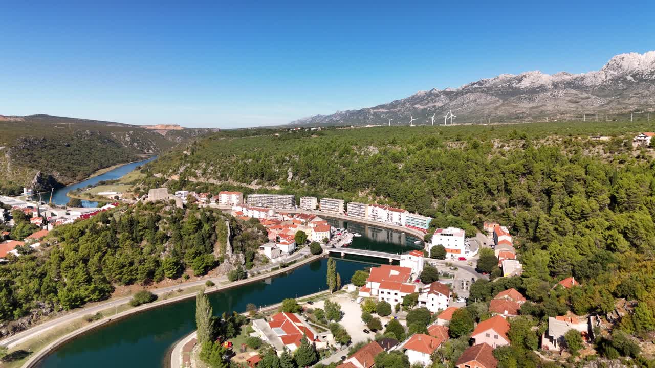 Bredt luftfoto over Obrovac — fra Velebit-bjergene til den S-formede Zrmanja-flod, der snor sig gennem den grønne natur og byen nedenfor. Dronebillede