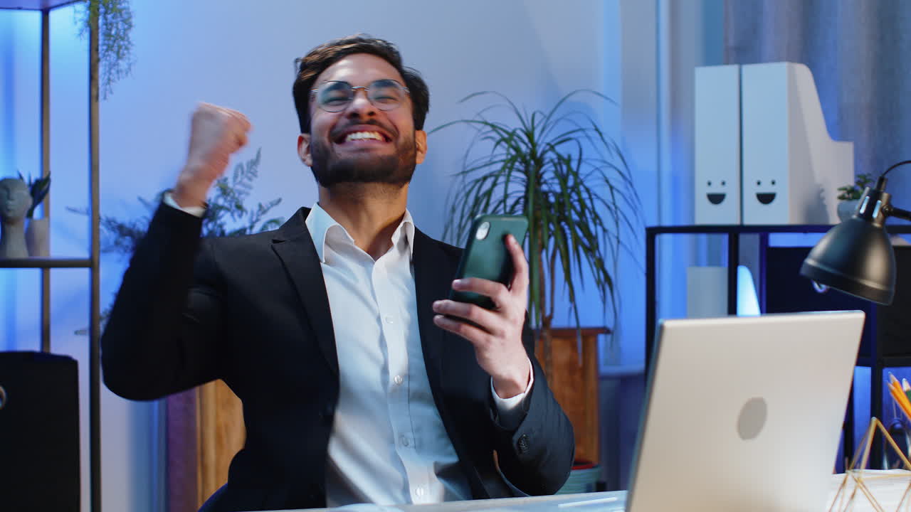 Happy indian businessman use smartphone celebrating success victory winning play online game
