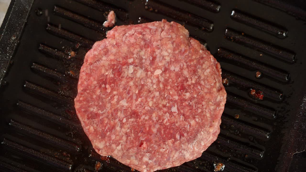 la mano de un hombre pone una hamburguesa cruda en la sartén.