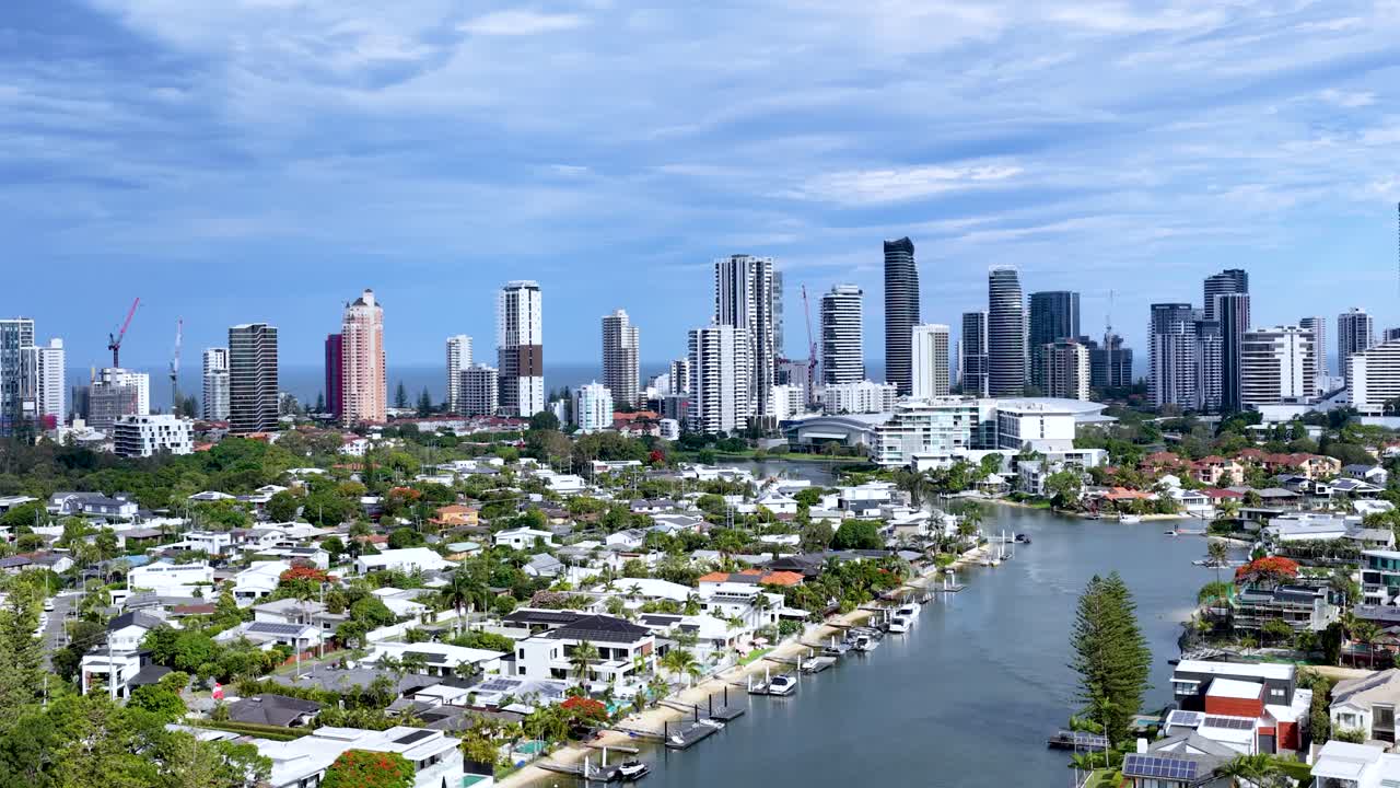 Drone glides above canal, revealing luxury homes, private docks, pools, and city skyline