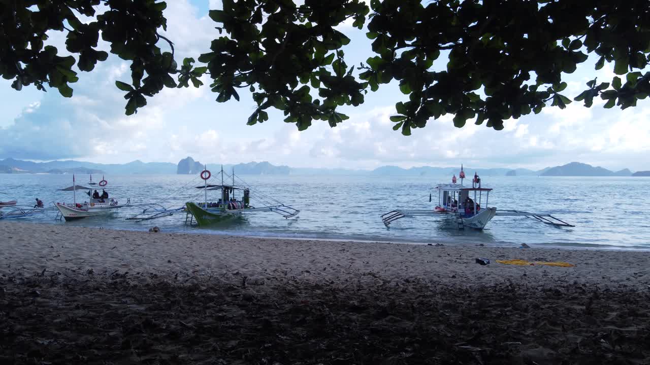 varios barcos de la banca filipina anclados en olas ligeras en la playa de arena blanca tropical