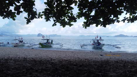 multiple filipino banca boats anchored in light waves at tropical white sand beach