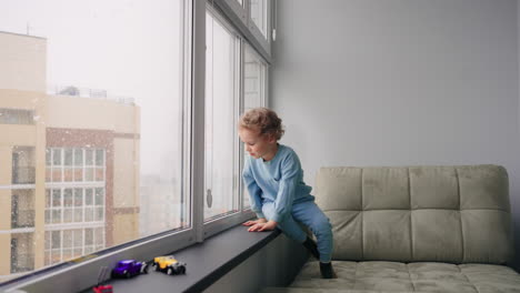 un niño travieso está jugando solo en la habitación en un día de invierno la nieve está cayendo detrás de la ventana el niño está sentado quieto