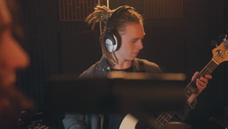 musical band records song in sound recording studio. male guitarist in headphones plays the electric guitar. close up of singer singing into microphone. music recording room. music production concept.