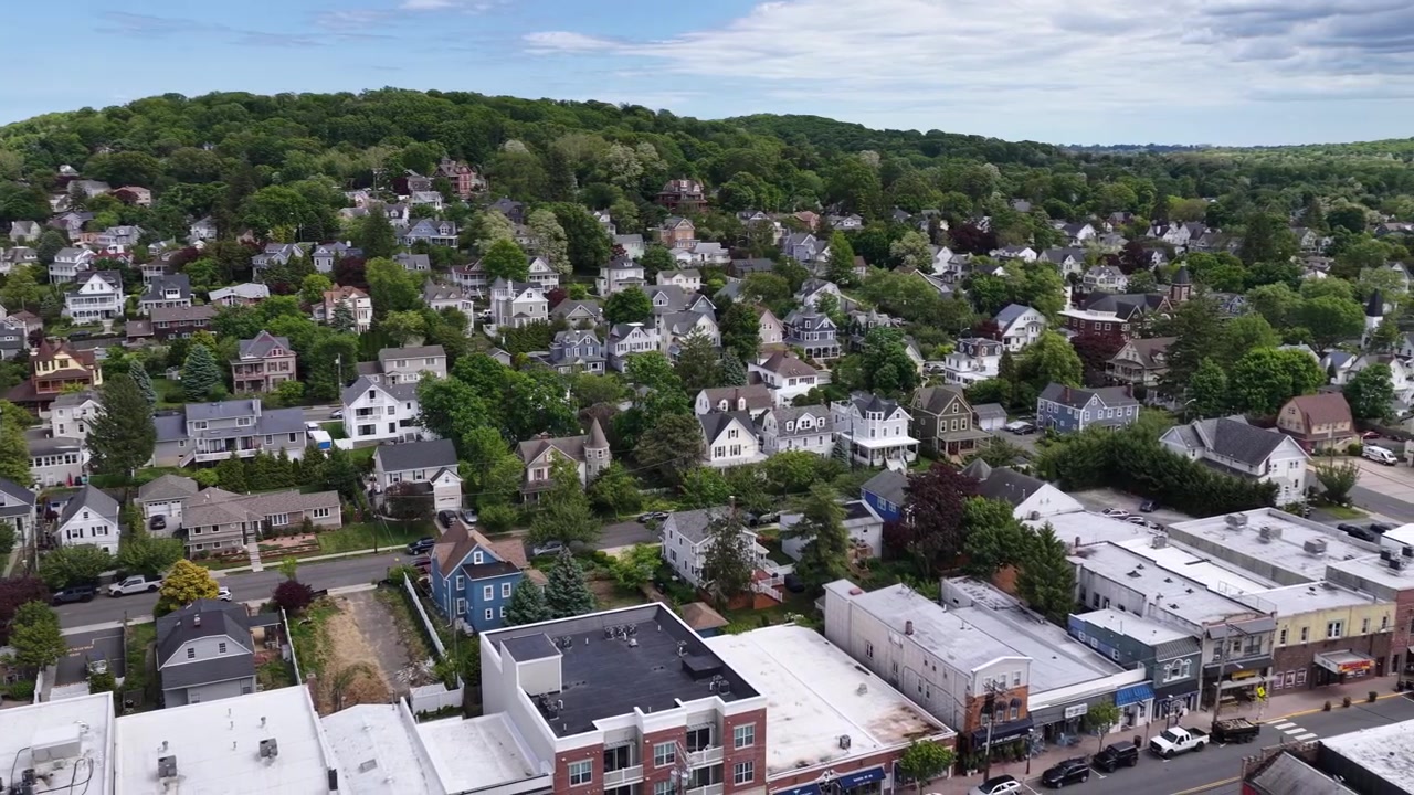 Veduta aerea di Atlantic Highlands, NJ, nella contea di Monmouth, che mostra case residenziali su un pendio verde sotto un cielo parzialmente nuvoloso e panoramica sulla via principale della città, First Avenue