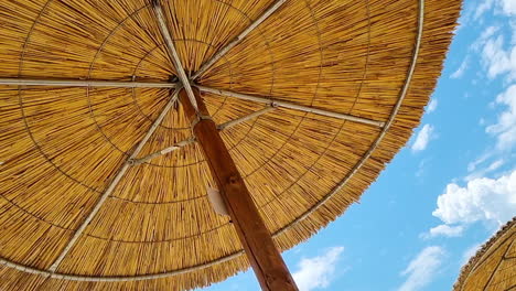 Bajo-La-Sombrilla-De-Playa-De-Paja-De-Caña-Y-El-Cielo-Azul-Claro-En-Un-Día-Soleado