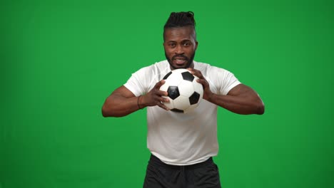focused african american man holding football ball looking at camera with serious facial expression. portrait of concentrated sportsman posing at chromakey green screen background. sportsmanship.