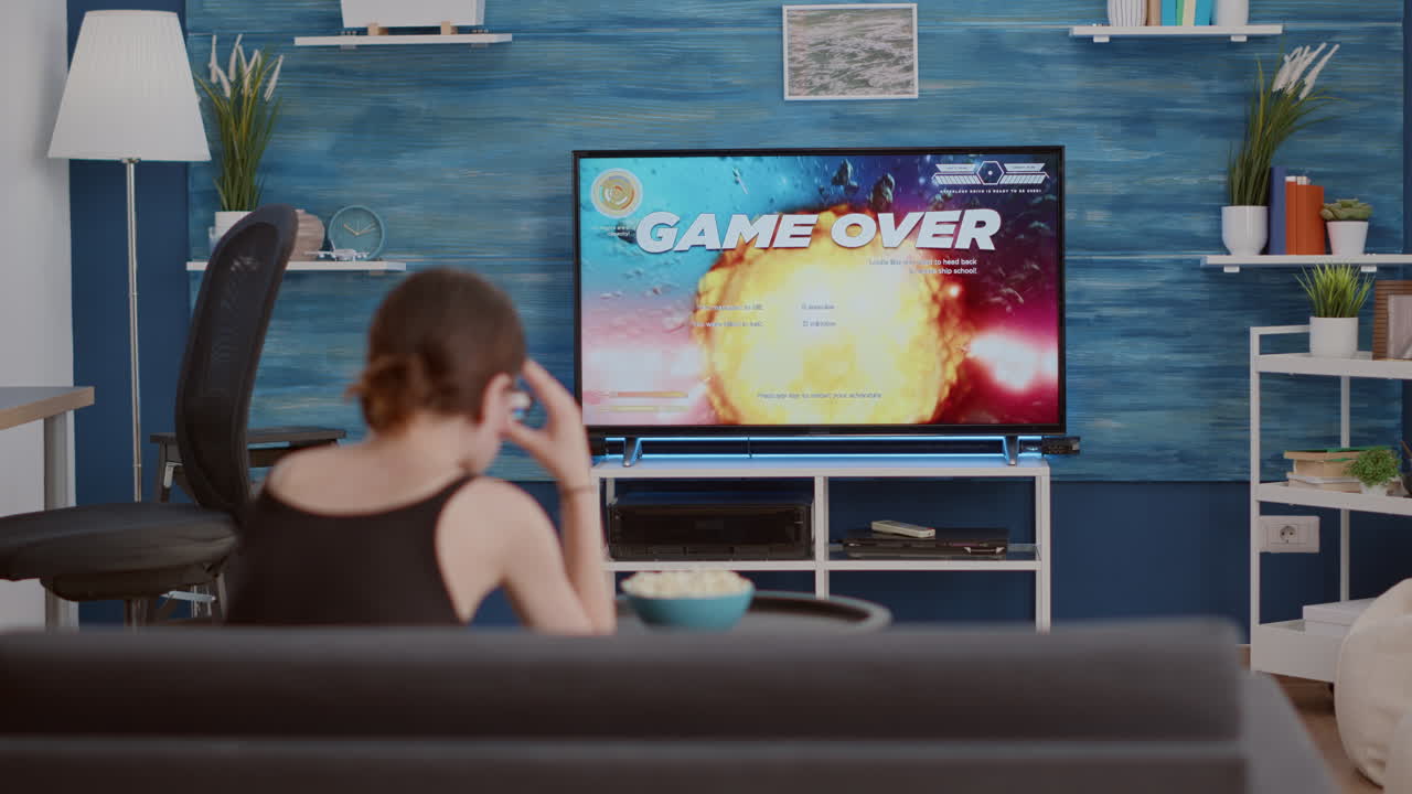 Young woman holding wireless controller playing action space shooter disappointed because losing online game