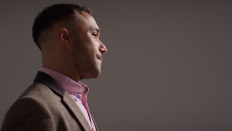 Side-View-Studio-Portrait-Of-Smiling-Mature-Male-Teacher-Wearing-Jacket-Standing-Against-Grey-Background-Shot-In-Slow-Motion