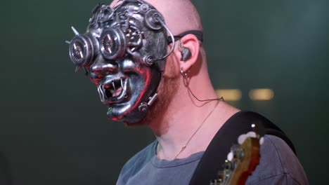 A man in a mask plays an electric bass guitar at a rock concert in a club. Nightlife in a big city. Red and blue lighting