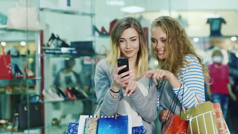 Dos-Atractivas-Mujeres-Mirando-Las-Fotos-En-El-Teléfono-En-Las-Manos-Tienen-Muchas-Bolsas-De-Compras-Smi