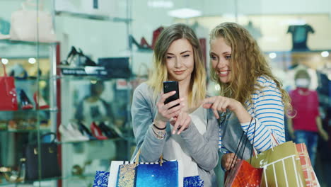 dos mujeres atractivas mirando las fotos en el teléfono en las manos tienen muchas bolsas de compras smi