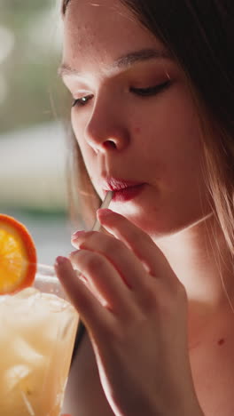 una joven bebe un cóctel a través de la paja en el bar. una mujer triste disfruta del sabor frutal descansando sola en el bar de la playa. un invitado sufre de soledad en una fiesta.