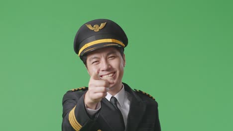 close up of asian man pilot smiling and touching his chest then pointing at you while standing in the green screen background studio