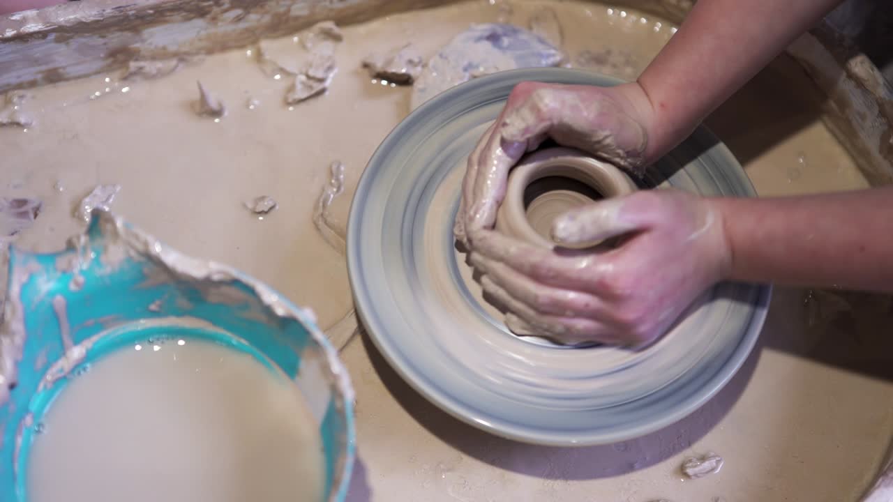 Top view of making of vase from clay. Stock footage. Close up of professional potter hands working with grey clay in workshop for making hand made pot.