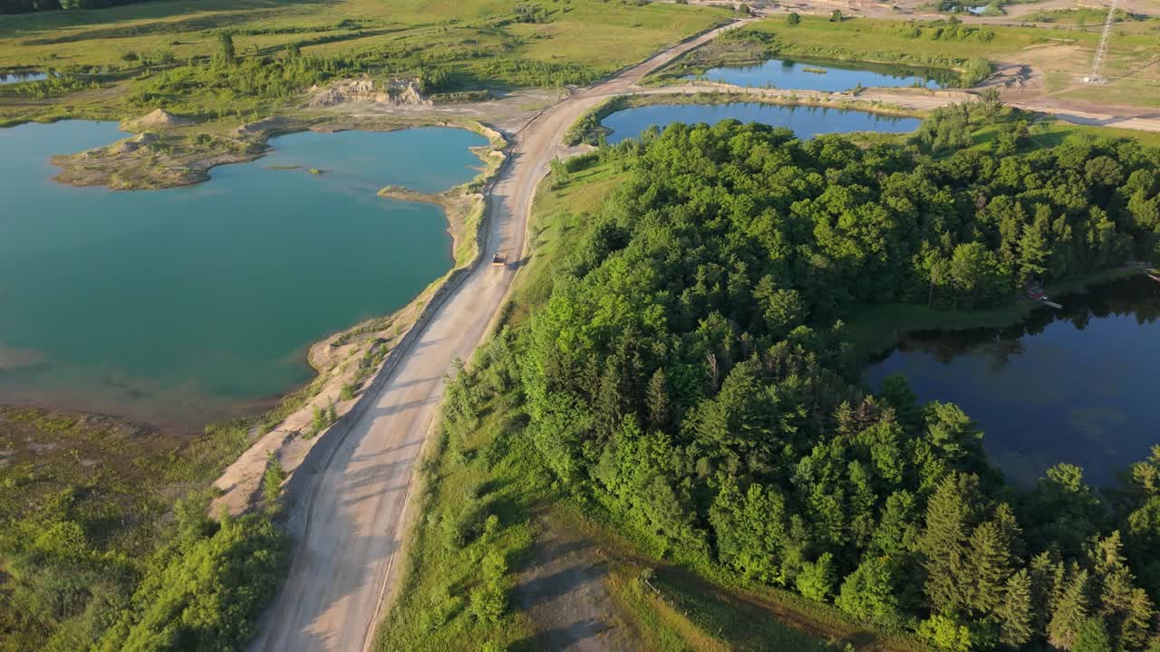 Aerial: gravel pit quarry lake and a dump truck during the day in Caledon, Ontario, Canada, pull out drone shot