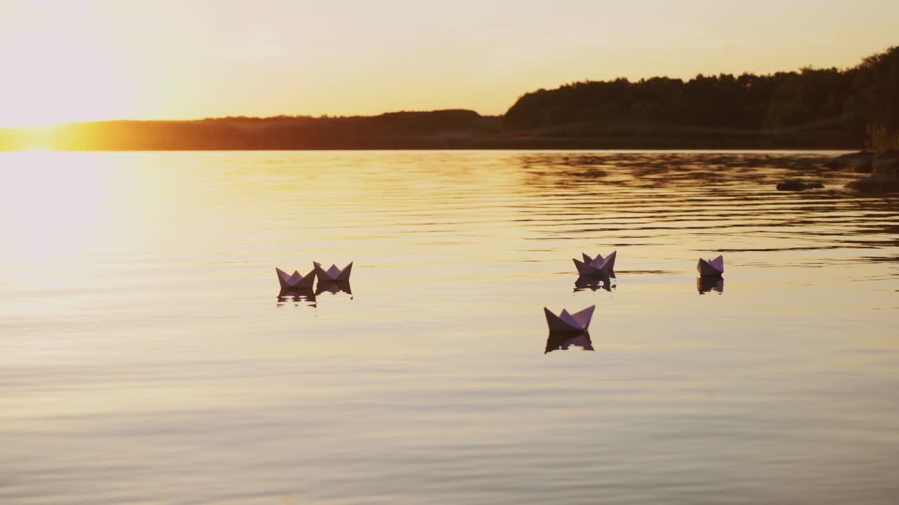 six origami in the form of boats sail by the lake at sunset in the evening. Paper boats are drifting with the flow of water far away