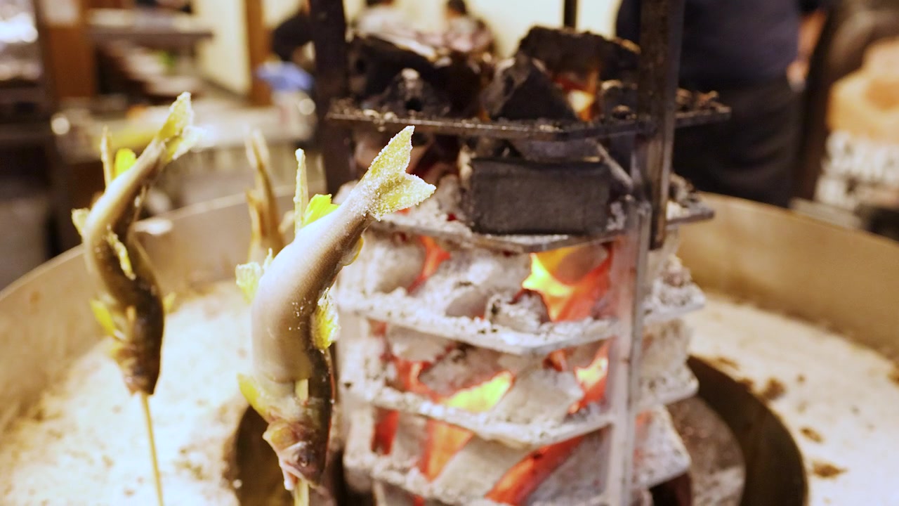 Close-up shot of whole fish on skewers grilling around a charcoal fire in Osaka