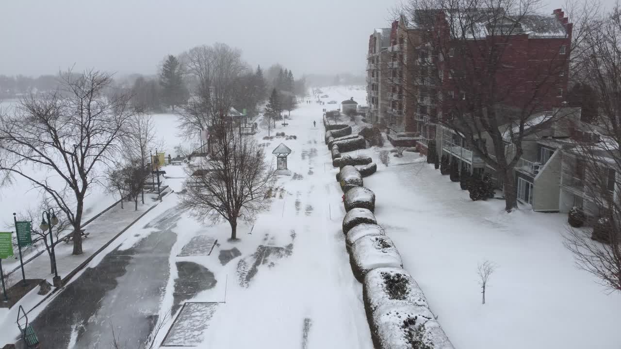Snow is heavily covering the promenade next to Memphremagog lake in Orford, Quebec, Canada, during a winter blizzard, with a hotel visible on the right