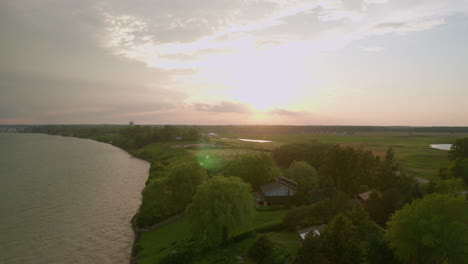 Drohnenansicht-Des-Sonnenuntergangs-Und-Der-Cottages,-Während-Vögel-Vorbeifliegen,-Mit-Grünem-Linseneffekt,-Der-Von-Der-Sonne-Gebrochen-Wird