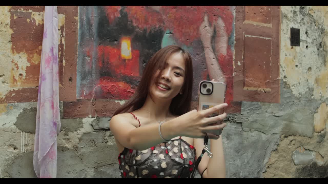 una chica guapa asiática sonríe y saluda en una videollamada en una pared mural en el barrio chino de malasia durante el día