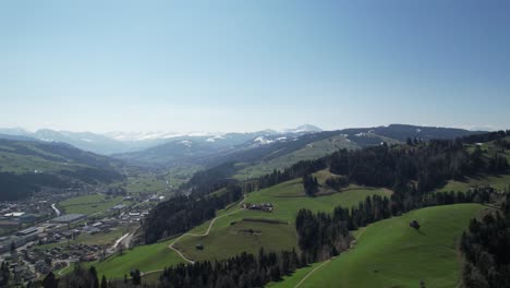 scenic aerial forward over green hills in switzerland, with city and mountains