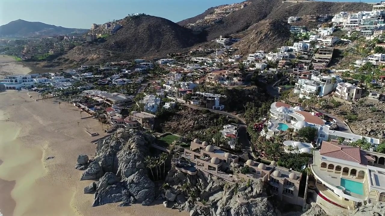 Drone vola dall'oceano sopra le case multimilionarie della comunità di Pedregal a Cabo San Lucas, con la spiaggia visibile per tutta la durata e girando alla fine per rivelare uno scorcio dell'oceano.