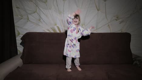 Little-cute-girl-with-blond-hair-jumps-on-sofa.-Bathrobe-clothes.-Happy