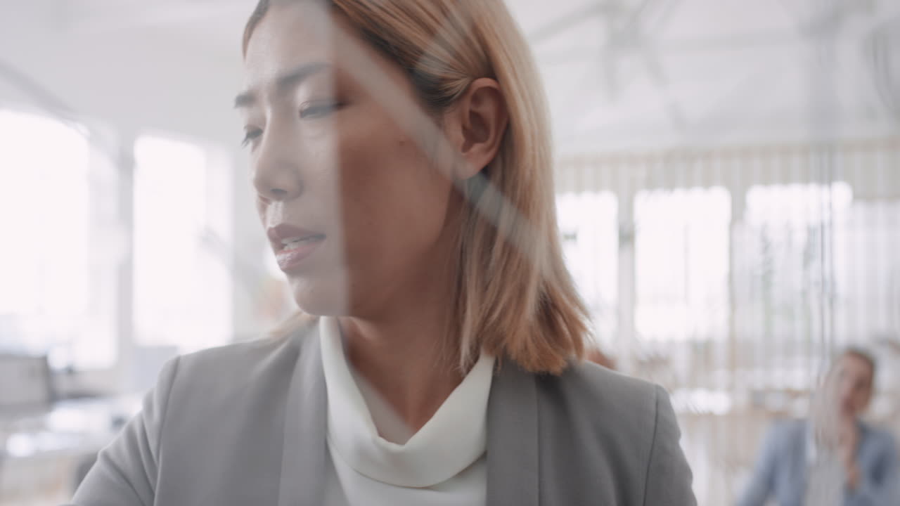 아시아의 비즈니스 여성 팀 리더가 유리 화이트보드에 글을 쓰고 동료들을 훈련시키고 기업 세미나 프레젠테이션에서 문제 해결 아이디어를 공유합니다.
