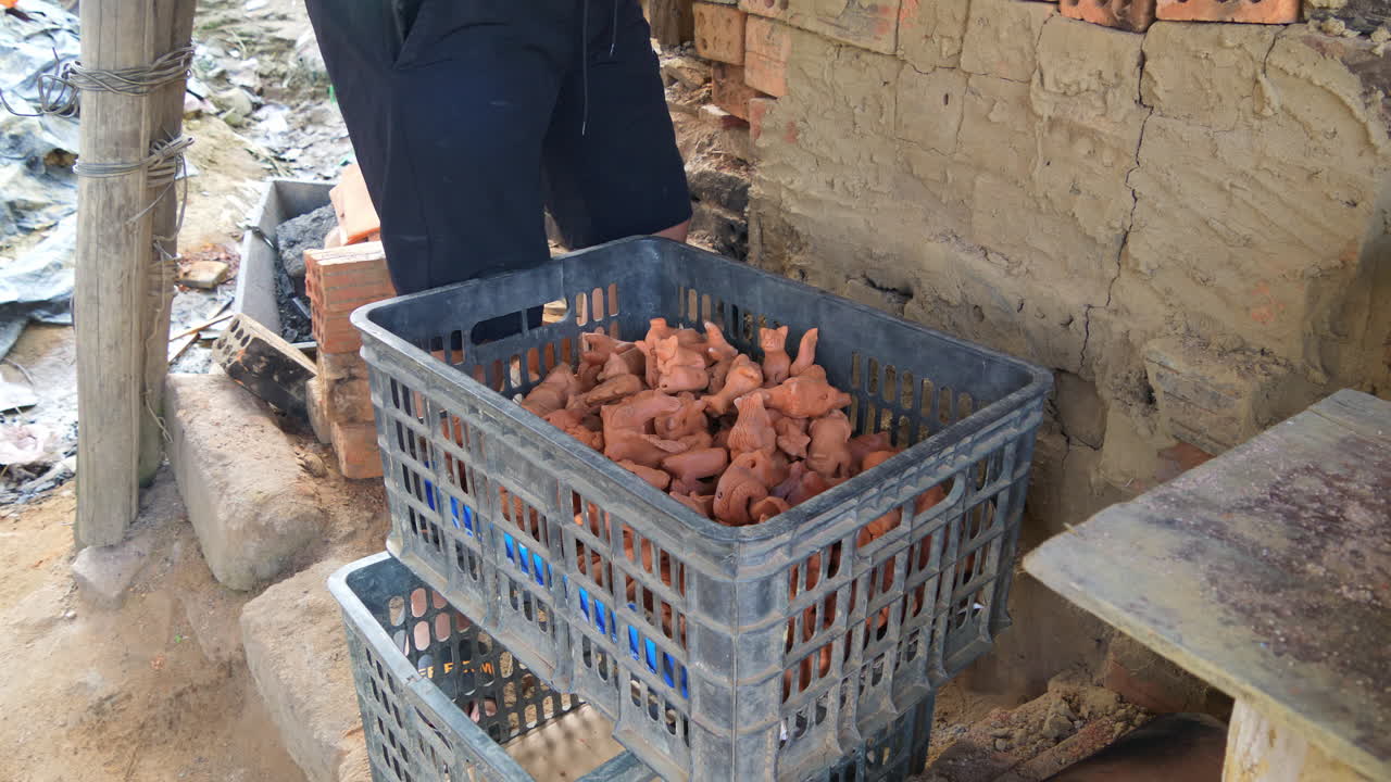 Low frontal side view of potter placing southeast asian clay figurines in basket, Than Ha Hoi An Vietnam