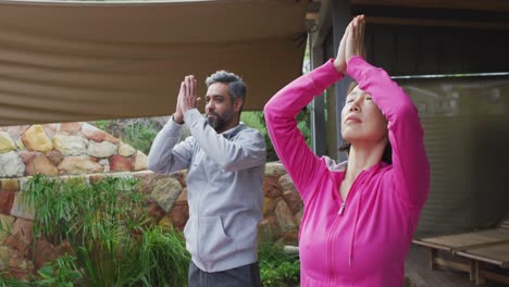 happy diverse couple doing yoga, standing and meditating at terrace