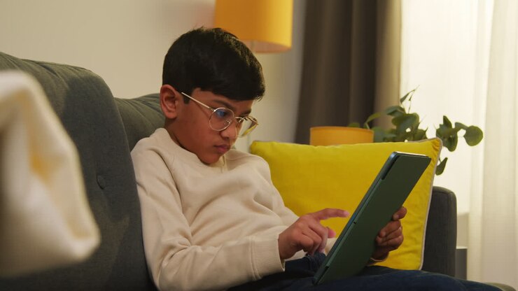 Giovane ragazzo seduto sul divano a casa, stanco di giocare o di guardare contenuti in streaming sul tablet digitale.