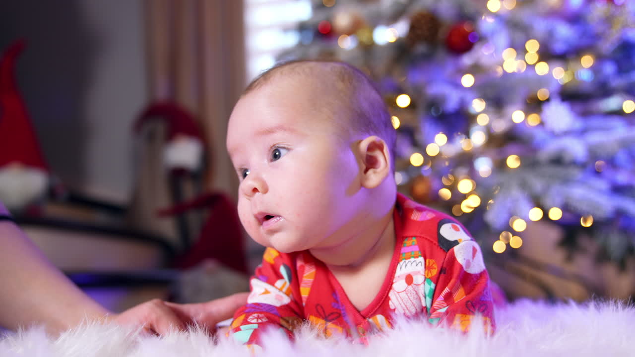 Beautiful Caucasian baby lies on the floor. Little boy is trying to hold his head and mommy supports the child.