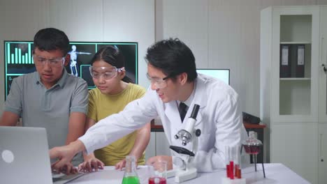 young asian boy and girl learning science experiment in laboratory with teacher in classroom, teacher explain with laptop computer