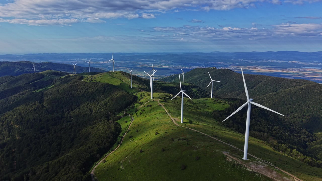 Turbine eoliche si ergono sulle colline sotto un cielo blu con nuvole.