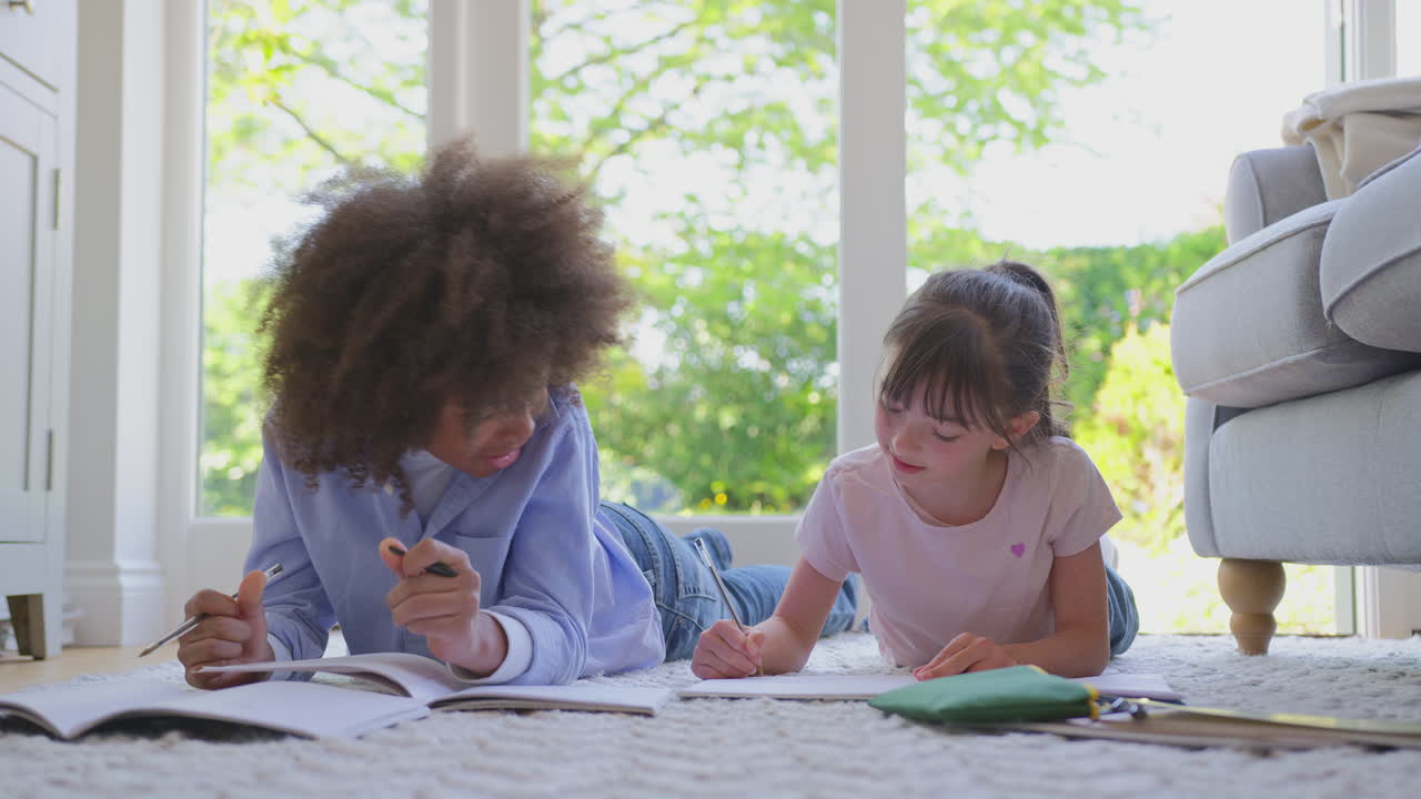 Boy And Girl Lying On Rug In Lounge At Home Doing School Homework Together