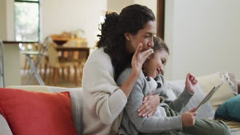 madre e hija de raza mixta felices sentadas en el sofá, divirtiéndose y usando la tableta