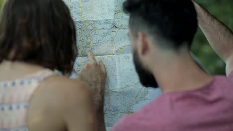 tourist couple looking at paper map, pointing finger at route location