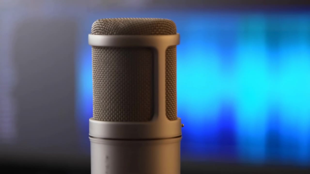 Large studio microphone in foreground shifts forward, partially covering bright blue and cyan waveform display on computer monitor, creating strong contrast in modern audio production workspace