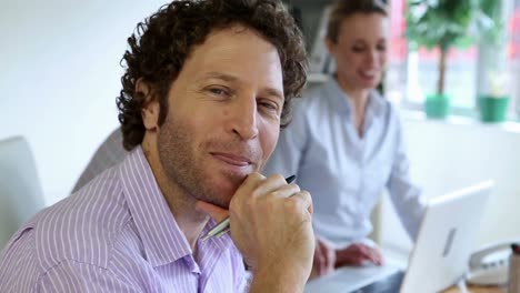 Businessman-smiling-at-camera-while-his-colleagues-are-chatting