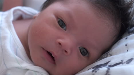 close up of cute newborn baby's face lying awake in bedroom