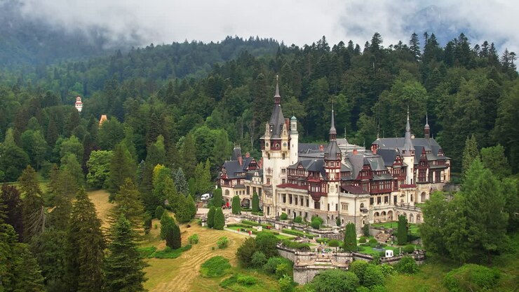 Vista aerea con drone del Castello di Peleș in Romania. Castello con giardini e turisti nei Carpazi, foresta lussureggiante tutt'intorno