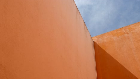 sunbeam shines through the concrete orange walls with blue sky and clouds above -tilt up shot