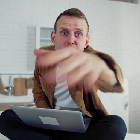 nervous businessman during quarantine. young man freelancer with a laptop sitting on a table in the kitchen and typing angrily. work at home during lockdown