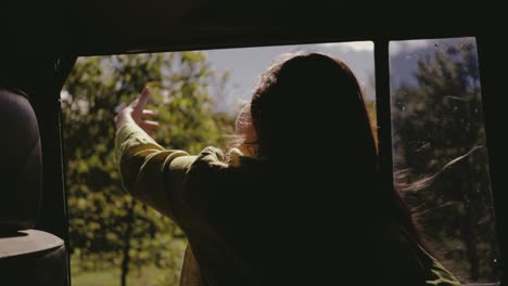 Eine-Frau,-Die-Den-Moment-Des-Sommers-Genießt,-Während-Ihr-Kopf-Durch-Das-Fenster-Eines-Autos-Hinausschaut,-Ihr-Haar-Im-Wind-Tanzt-Und-Ihre-Hand-Draußen-Spielt