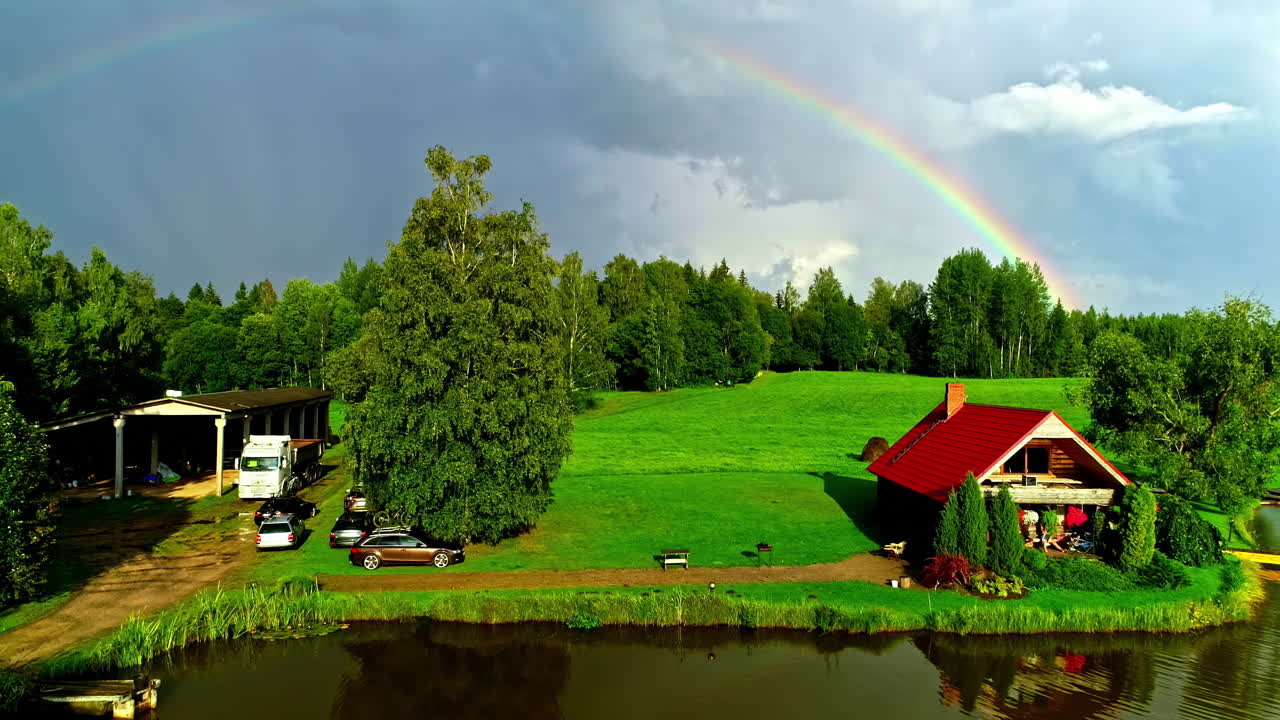Cozy Lakeside Cabin by Pond with Rainbow Arching Over Lush Green Countryside Setting